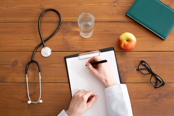 Recommendations and prescription from doctor. Woman in white coat writes on tablet at workplace - Foto, imagen
