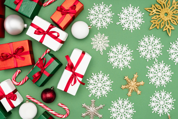 top view ajándékdobozok, karácsonyi labdák, cukornád és dekoratív hópelyhek zöld háttér - Fotó, kép