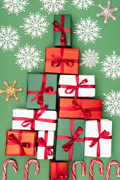 vista superior de cajas de regalo multicolores con cintas rojas y copos de nieve decorativos sobre fondo verde - Foto, imagen