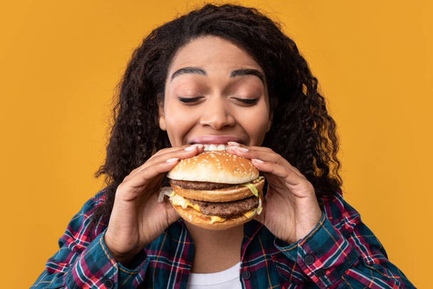 Primo piano di divertente nero signora mangiare hamburger a studio - Foto, immagini