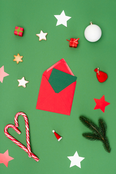 top view piros boríték kártyával közel karácsonyi baubles, sült csillagok és cukornád zöld - Fotó, kép