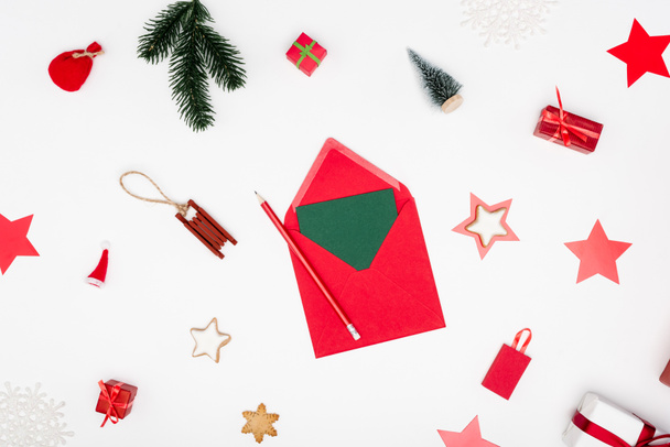 top view of red envelope with card and pencil near christmas baubles and baked stars on white - Photo, Image