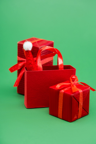 red gift boxes and shopping bag with santa hat on green background - Foto, afbeelding