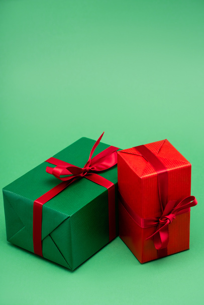 δύο πολύχρωμα κουτιά δώρου με κόκκινες κορδέλες και φιόγκους σε πράσινο φόντο - Φωτογραφία, εικόνα