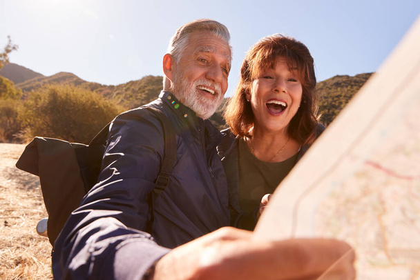 Senior Couple Looking At Map As They Hike Along Trail In Countryside Together - Foto, Bild