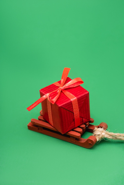red gift box on decorative wooden sleigh on green background - Φωτογραφία, εικόνα