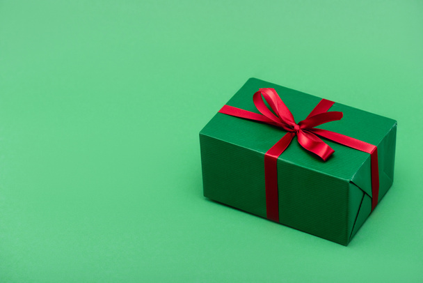 colorful gift box with red ribbon and bow on green background with copy space - Фото, изображение