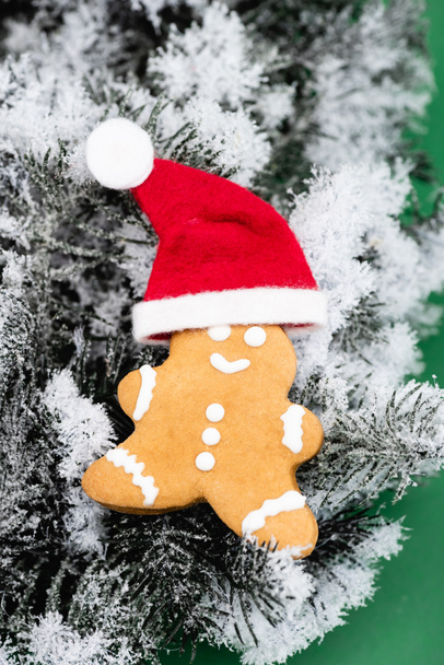 Lebkuchenmann mit Weihnachtsmütze auf Tannenzweig mit dekorativem Schnee - Foto, Bild
