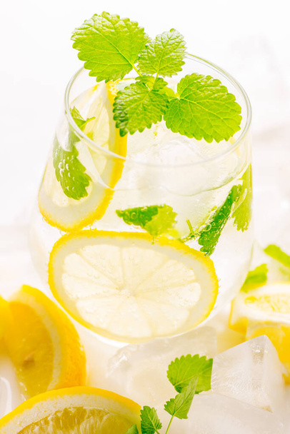 Lemonade drink in a glass: water, ice, lemon slice and mint on white background - Photo, Image