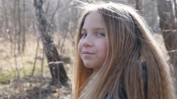 Πορτρέτο του ευτυχισμένου μικρού παιδιού με φόντο το θολό φόντο ενός δάσους στις αρχές της άνοιξης. Χαμογελαστό ξανθό κορίτσι κοιτάζει στην εξωτερική κάμερα. Κοντινό πλάνο συναισθήματα του γυναικείου παιδιού με ευχάριστη έκφραση στο πρόσωπο - Πλάνα, βίντεο