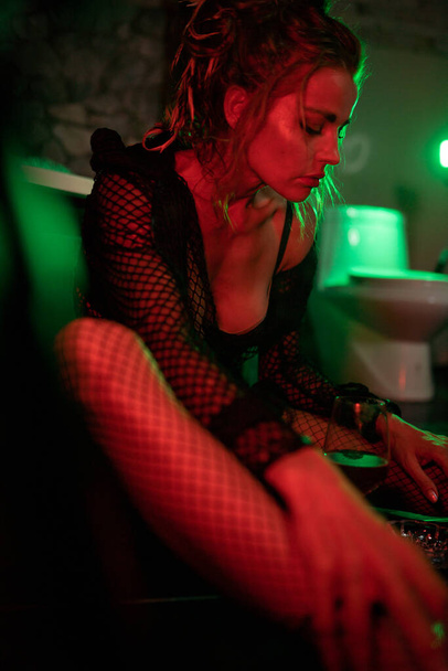 Sexy woman sitting on the floor in bathroom, smoking and drinking wine. Red and gren light. Cinematic shot - Φωτογραφία, εικόνα