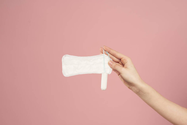 Beschermende pad en tampon in vrouwelijke handen op een roze achtergrond menstruatie kritieke dagen - Foto, afbeelding