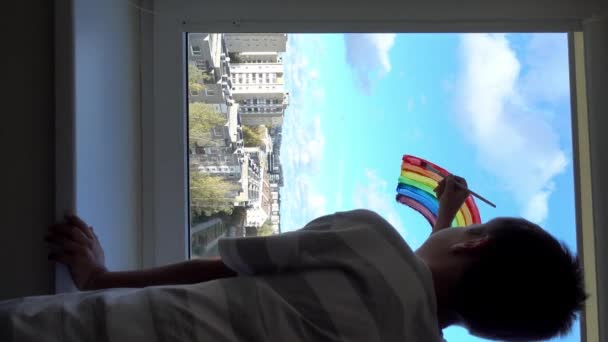 Αγόρι ζωγραφική πολύχρωμο ουράνιο τόξο στο παράθυρο κατά τη διάρκεια της καραντίνας Covid-19 στο σπίτι. Μείνετε στο σπίτι λόγω του κινδύνου μόλυνσης από τον ιό της στέψης. Σύμβολο ελπίδας. 4ια - Πλάνα, βίντεο
