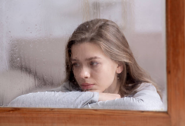 Onneton nuori nainen katselee ulos ikkunasta pisaroita sade, tunne surullinen tai melankolinen - Valokuva, kuva