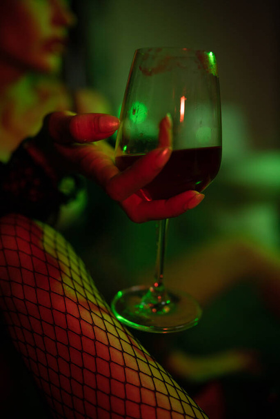 Sexy woman sitting on the floor in bathroom, smoking and drinking wine. Red and gren light. Cinematic shot - Photo, Image