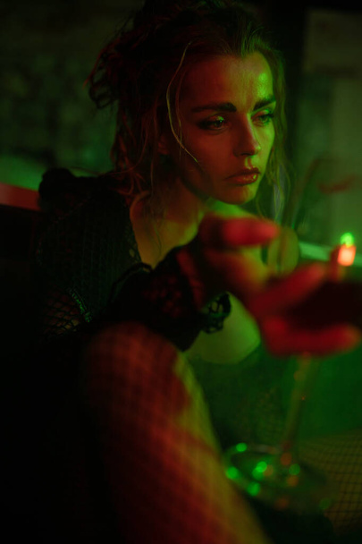セクシーな女性がバスルームで床に座って、喫煙やワインを飲む。赤と緑の光。シネマティック・ショット - 写真・画像