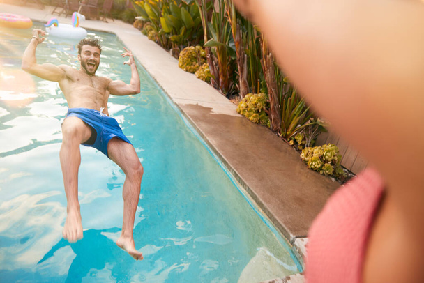 Hispanic Couple With Woman Pushing Man Into Swimming Pool At Outdoor Summer Party - 写真・画像