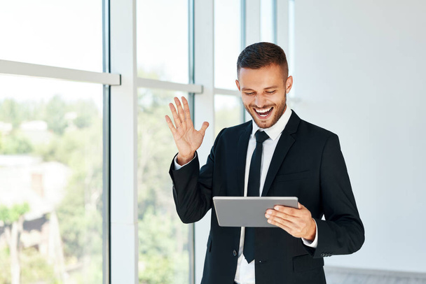 Happy successful businessman in elegant suite reading good news using tablet in modern creative office background - Zdjęcie, obraz