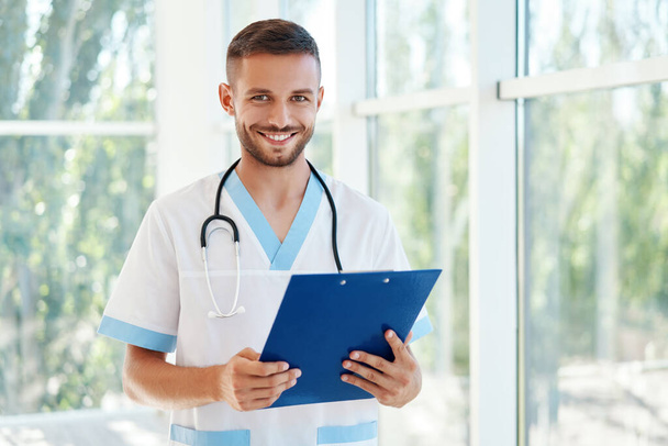 Portrait of confident male doctor with stethoscope and clipboard in medical uniform - Foto, Bild