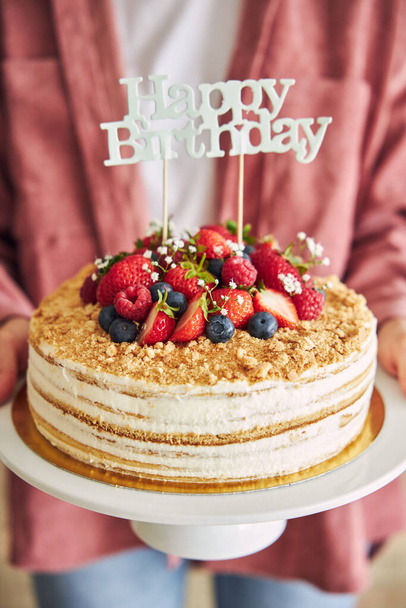 Eine Nahaufnahme einer Person, die den fruchtigen Kuchen mit einem "Happy Birthday" Topper hält - Foto, Bild