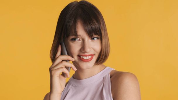 Jolie fille brune souriante avec des cheveux de bob parler avec le meilleur ami au téléphone sur fond coloré - Photo, image
