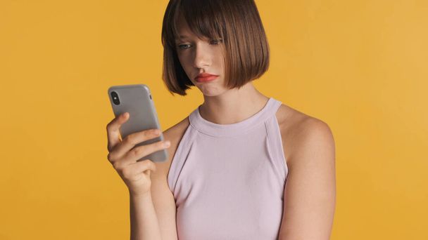 Aufgebracht brünettes Mädchen mit Bob-Haaren traurig aussehen erhalten Nachricht von Freund auf Smartphone über bunten Hintergrund - Foto, Bild