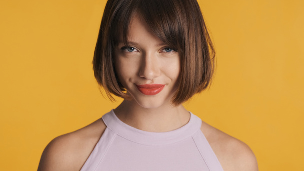 Charming flirty brunette girl with bob hair and red lips slyly looking in camera isolated on yellow background - Photo, Image