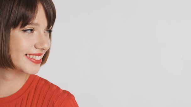 close-up mooi brunette meisje met rode lippen op zoek naar plaats voor reclame of promotionele tekst en glimlachen over witte achtergrond - Foto, afbeelding