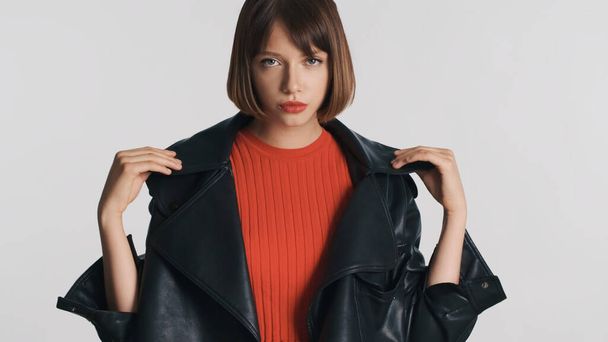 Beautiful brunette girl with bob hair and red lips dressed in leather jacket posing on camera over white background - 写真・画像