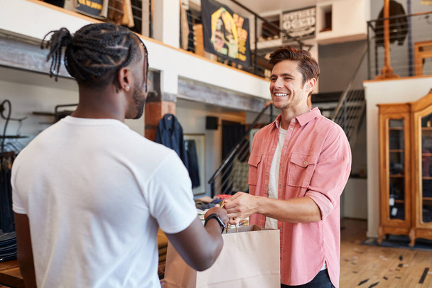 Verkäuferin übergibt Einkäufe an männlichen Kunden im Modegeschäft - Foto, Bild