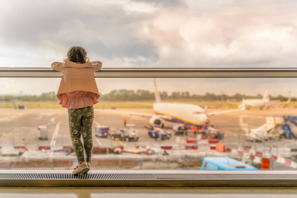 Silueta de niña en la terminal del aeropuerto. De pie en el alféizar de la ventana y mirando en los aviones, esperando la salida. Dublín, Irlanda - Foto, imagen