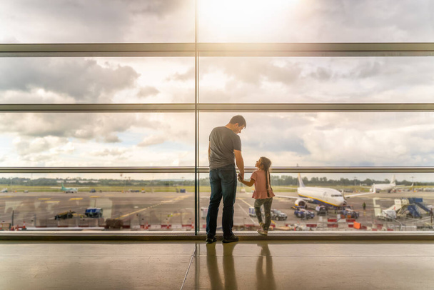 Silhouette von Familie, Vater und Tochter auf dem Flughafenterminal. Händchenhaltend und einander anschauend, wartend auf die Abreise. Dublin, Irland - Foto, Bild