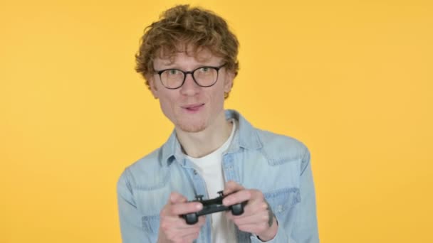 Redhead νεαρός άνδρας που παίζει βιντεοπαιχνίδι, κίτρινο φόντο  - Πλάνα, βίντεο