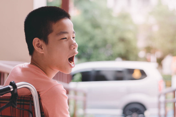 Tekerlekli sandalyede tekerlekli sandalyede bekleyen özel Asyalı çocuk park yerinde engelli insanlar, eğitim çağında yaşam ve engelli çocukların toplu taşımacılığı, Mutlu Özel Çocuklar konsepti. - Fotoğraf, Görsel