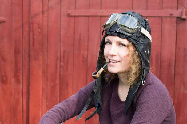 Портрет девушки на винтажном мотоцикле в пилотной кепке с дымящейся трубкой - Фото, изображение