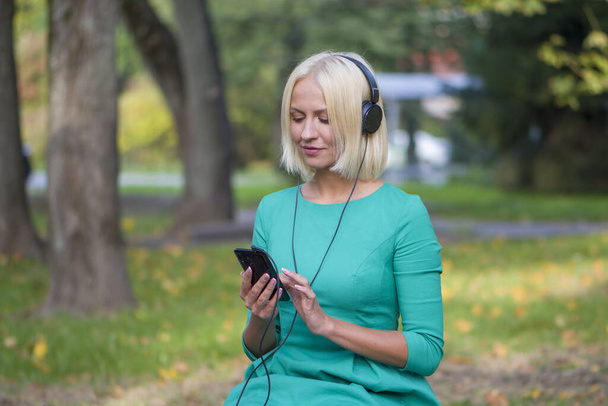 Eine junge Frau zwischen 25 und 30 Jahren im Park hört Musik mit Kopfhörern von ihrem Handy und konzentriert sich selektiv. - Foto, Bild