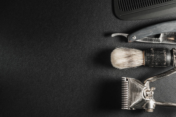 On a black surface are old barber tools.Two vintage manual hair clipper, comb, razor, shaving brush, hairdressing scissors. black monochrome. Close-up. Barbershop background. contrast shadows. Horizontal orientation. Top view, flat lay. copy space - Photo, Image