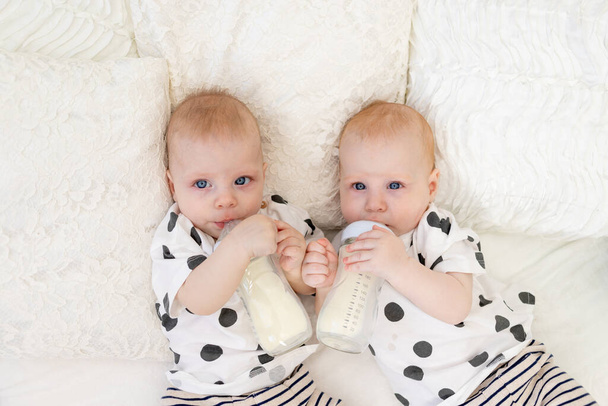 dos gemelos hermanos y hermanas de 8 meses de edad yacen en la cama en pijama y beben leche de un biberón, concepto de comida para bebés, vista superior, concepto de amistad, lugar para el texto - Foto, Imagen