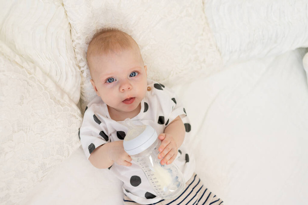 Baby 8 months old lying on the bed in pajamas and drinking milk from a bottle, baby food concept, top view, place for text - Фото, изображение