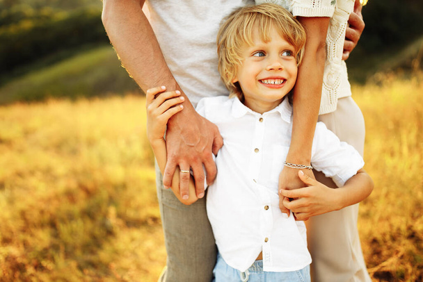 Joyful preschooler boy holding caring parents arms, smiling, happy child with mother and father at the field, family spend time together, childhood and parenthood concept - Foto, Imagem