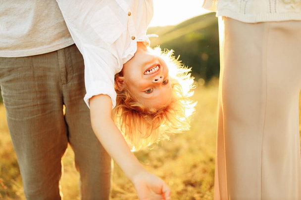 Portrait of preschool boy upside down, strong father hold joyful son, happy parents with smiling kid at the field, lovely family making fun, spend time together, childhood concept - Φωτογραφία, εικόνα