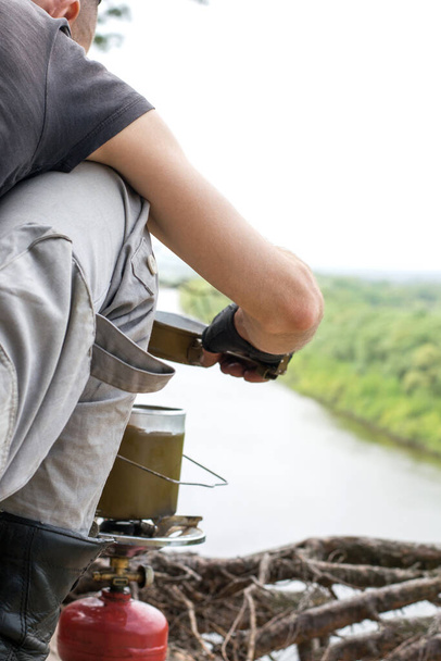 Traveler prepares for a gas burner food over cliff above the river - Valokuva, kuva