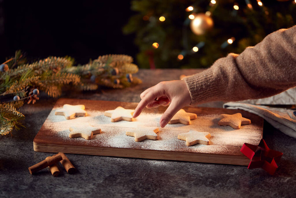 Womans Hand Reaches For Freshly Baked Star Shaped Christmas Cookies On Board Dusted With Icing Sugar - Foto, Bild