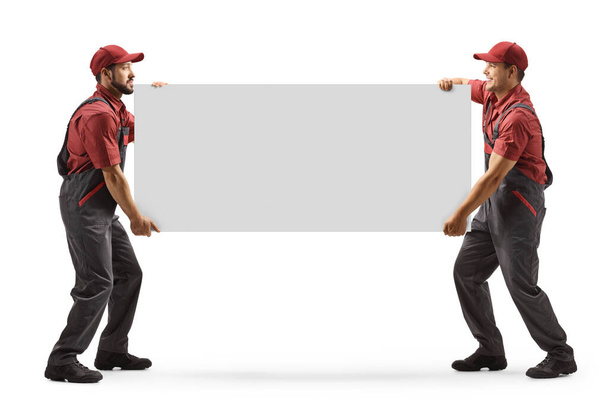 Full length shot of two male workers carrying a blank panel board isolated on white background - Zdjęcie, obraz