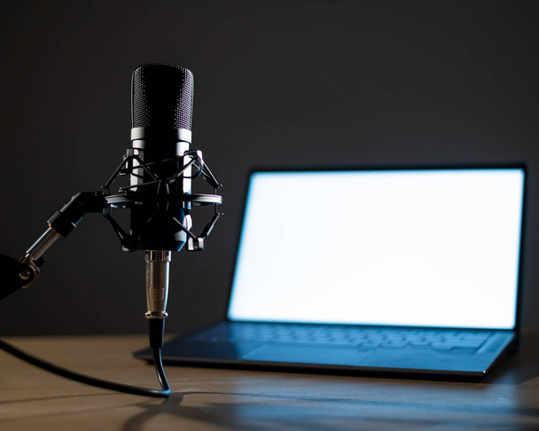 Professional microphone and laptop with white screen in the dark. Equipment in a recording and broadcasting studio - Fotó, kép
