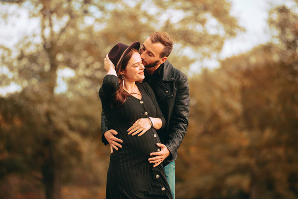 Μια φωτογραφία μιας υπέροχης νεαρής οικογένειας με μια έγκυο στο πάρκο. - Φωτογραφία, εικόνα