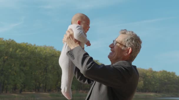 Dziadek trzymający dziecko w ramionach na zewnątrz. Więzi między dziadkami a wnukami. - Materiał filmowy, wideo