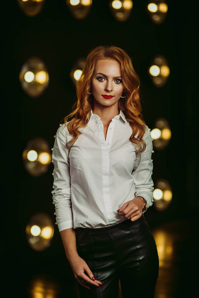 Business Woman in a white shirt against the background of burning lamps in the interior of a dark Studio.Model with long hair and red lipstick - Fotografie, Obrázek