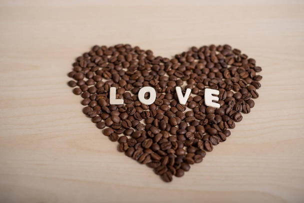 Coffee beans in the shape of a heart and the inscription love on a wooden table - Fotografie, Obrázek