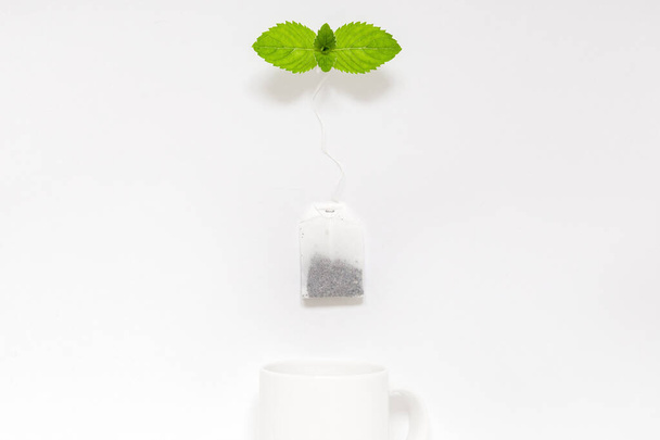 Tea bag with fresh mint above the white mug in a flat lay. Tea break concept - Fotografie, Obrázek